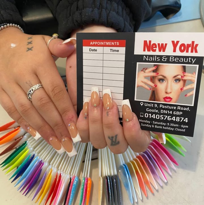 Nude French tips with gems held over a fan of colour swatches